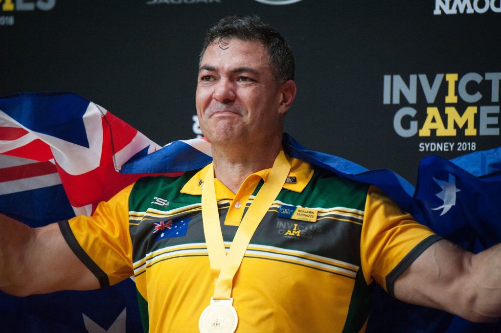 male veteran holding Australian flag and wearing gold medal