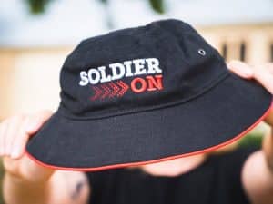 Black bucket hat with red piping on the hem and Soldier On logo in white and red.