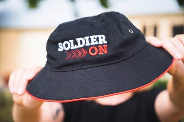 Black bucket hat with red piping on the hem and Soldier On logo in white and red.