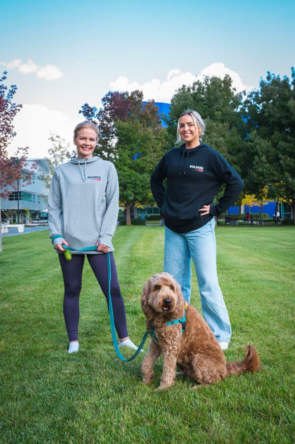 Grey and black hoodie with Soldier On logo on left hand chest worn by two women with a dog.