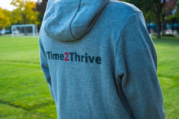 Back of a light grey hoodie with text that reads hashtag time two thrive in dark grey and red.