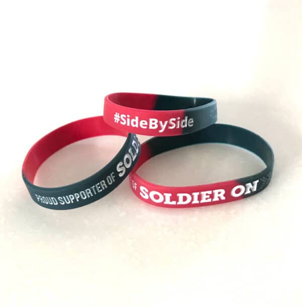 Three dark grey and red wristbands with the text side by side and proud supporter of Soldier On on them.