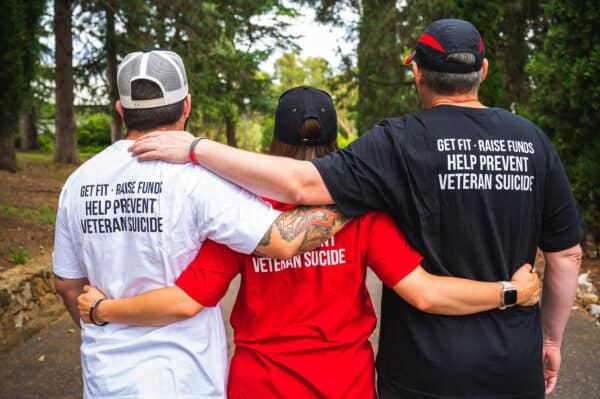 Three people stand with their arms around each other showing the back of March On tee shirts in white, red and black.