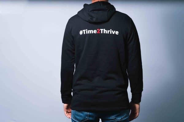 View of the whole back of the black hoodie with hashtag time two thrive text in white and red across the top of the hoodie.