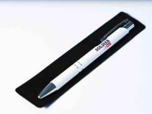 White pen with dark grey and red Soldier On logo, and silver accents. The pen sits on top of a black velvet pouch.