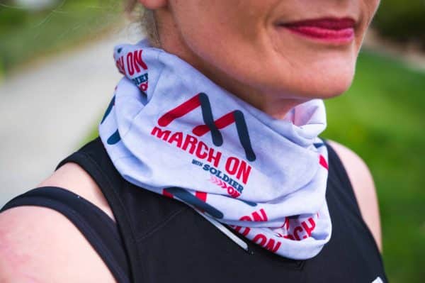 Close up of light grey neck sock with the March On with Soldier On logo in dark grey and red, worn on the neck of a woman.