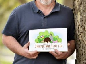 The author stands leaning against a tree holding a picture book.